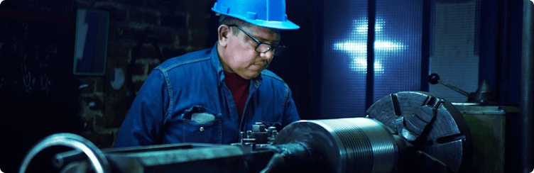 Factory worker operating machinery with sparks in an industrial setting.