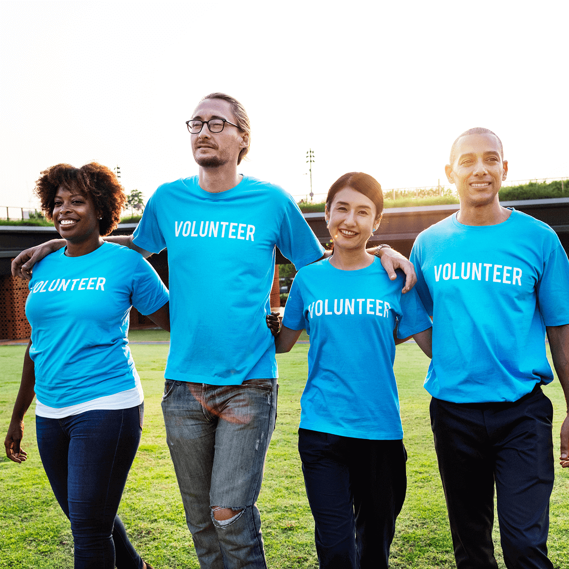 Four volunteers in blue ‘VOLUNTEER’ shirts walking outdoors with arms around each other.