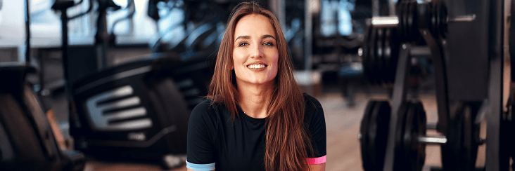 Smiling woman in athletic wear seated in a gym setting.